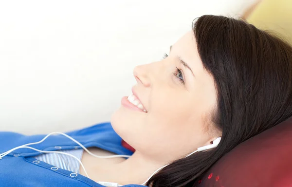 Sonriente chica adolescente escuchando música tumbada en un sofá —  Fotos de Stock