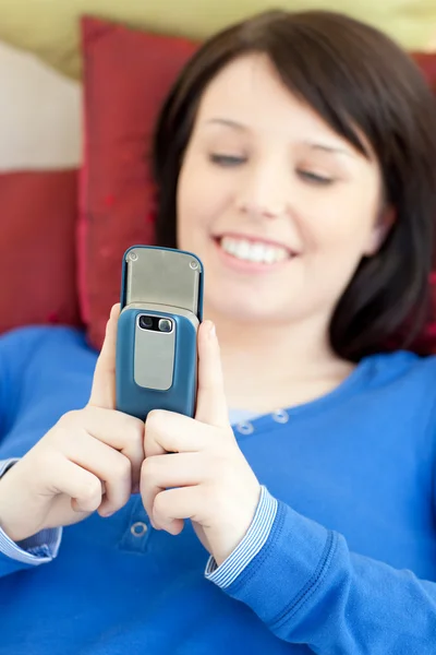 Fröhliches Teenie-Mädchen schickt einen Text, der auf einem Sofa liegt — Stockfoto