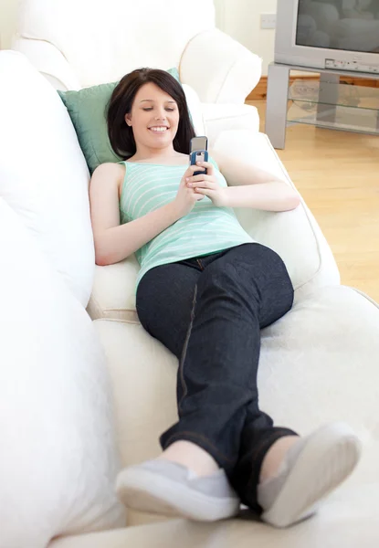 Vrolijke vrouw verzenden van een tekst liggen op een sofa — Stockfoto