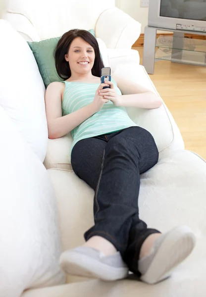 Mujer alegre enviando un mensaje de texto acostado en un sofá —  Fotos de Stock