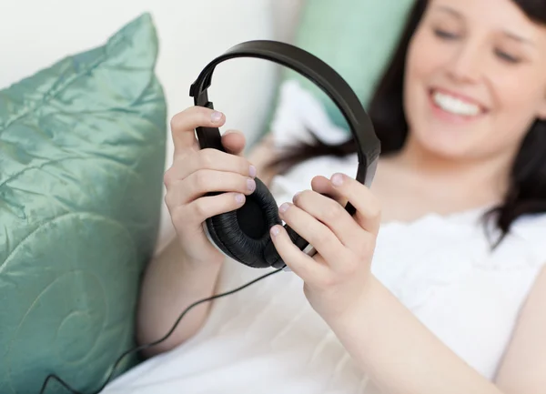 Εύθυμη νεαρή γυναίκα βάζει ακουστικά ξαπλωμένη σε ένα καναπέ — Φωτογραφία Αρχείου