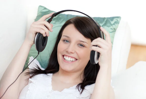 Mulher alegre colocando fones de ouvido deitado em um sofá — Fotografia de Stock