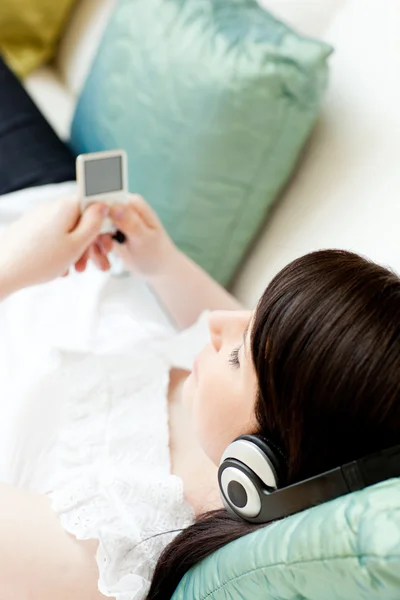 Brunetka dama słuchania muzyki, leżąc na kanapie — Zdjęcie stockowe