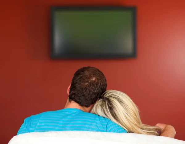 Пара, сидящая на диване и смотрящая телевизор дома — стоковое фото