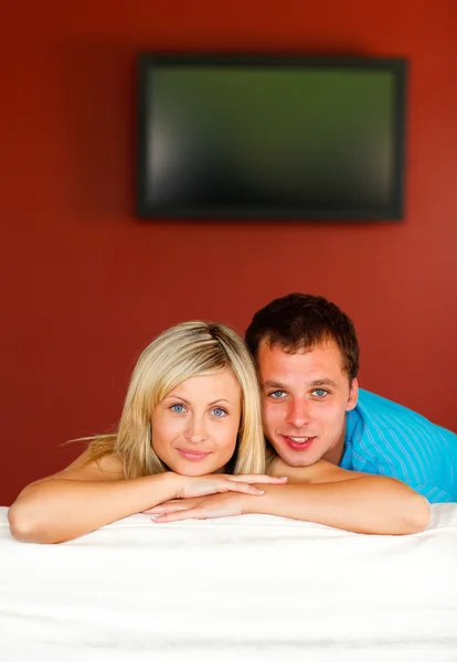 Couple sitting on couch with television in the background — Stock Photo, Image