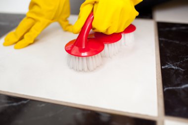 A person cleaning a bathroom's floor with a yellow rubber glove clipart