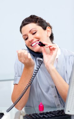 Smiling woman on phone painting her nails clipart