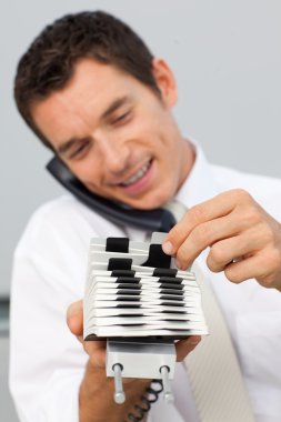 Businessman on phone and consulting a card holder clipart