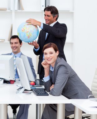 Happy manager holding a globe with his team working at computers clipart