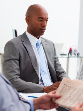 Businessman reading a newspaper with his colleague workig at a c clipart