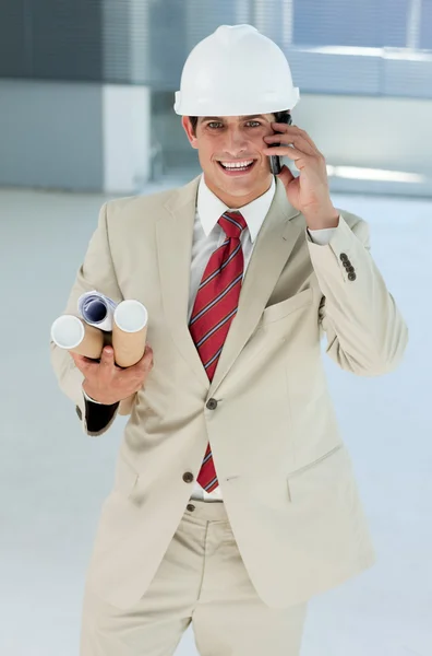 Χαμογελώντας αρσενικό αρχιτέκτονα με ειδικό κράνος στο τηλέφωνο — Φωτογραφία Αρχείου
