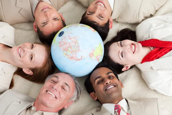 Um negócio diversificado deitado no chão em torno de um globo — Fotografia de Stock