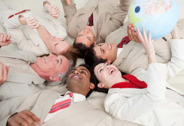 Equipe de negócios deitada no chão brincando com uma glob terrestre — Fotografia de Stock