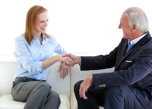 Smiling business shaking hands sitting on a sofa — Stock Photo, Image