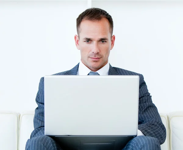 Homem de negócios concentrado usando um laptop sentado em um sofá — Fotografia de Stock