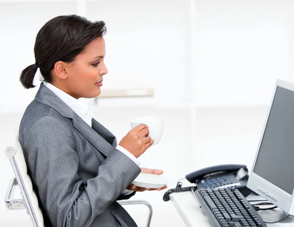 Attraktiva affärskvinna dricka en kaffe medan du arbetar på en com — Stockfoto
