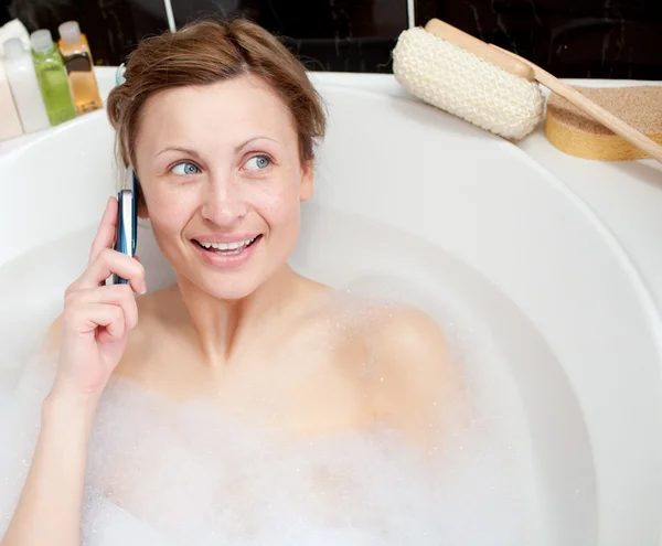 Femme rayonnante parlant au téléphone dans un bain moussant — Photo