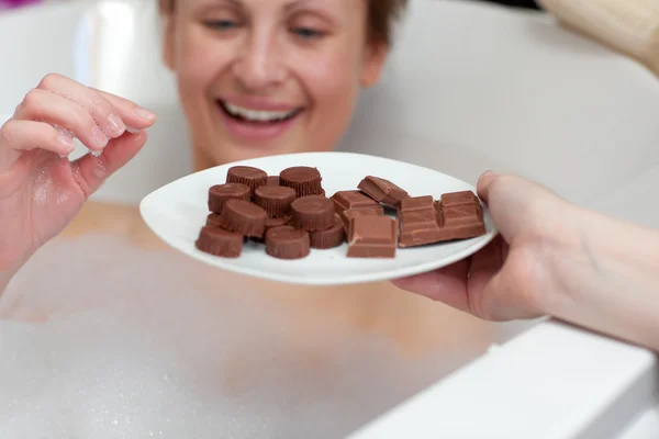 Vrolijke jonge vrouw die het eten van chocolade terwijl het hebben van een bad — Stockfoto