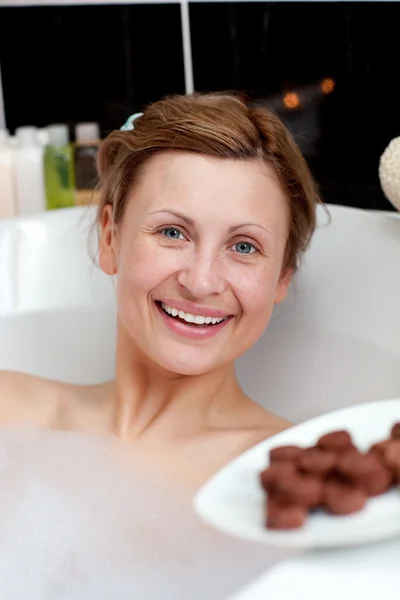 Femme rayonnante manger du chocolat tout en prenant un bain — Photo