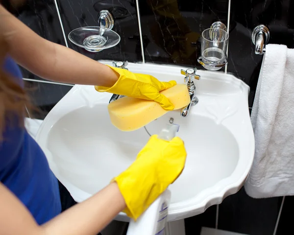 Jovem mulher limpando a pia de um banheiro — Fotografia de Stock