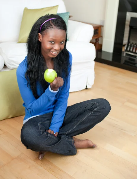 Gelukkige vrouw eten een appel zittend op de vloer — Stockfoto