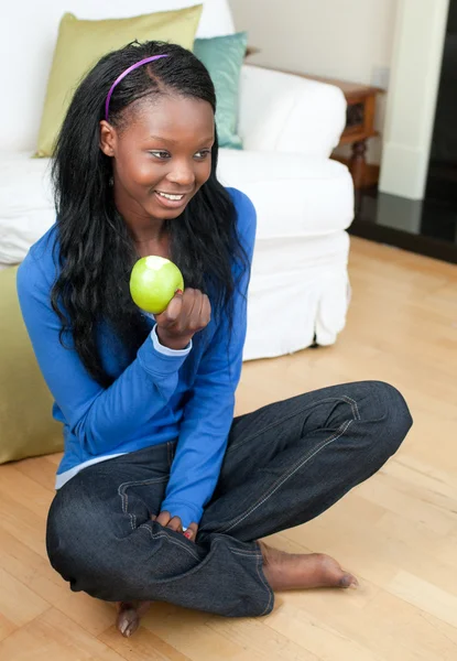 Веселая женщина ест яблоко, сидя на полу — стоковое фото