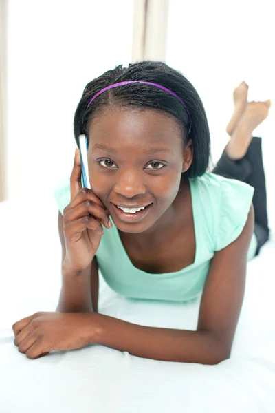Lächelndes Teenie-Mädchen mit einem Handy, das auf ihrem Bett liegt — Stockfoto