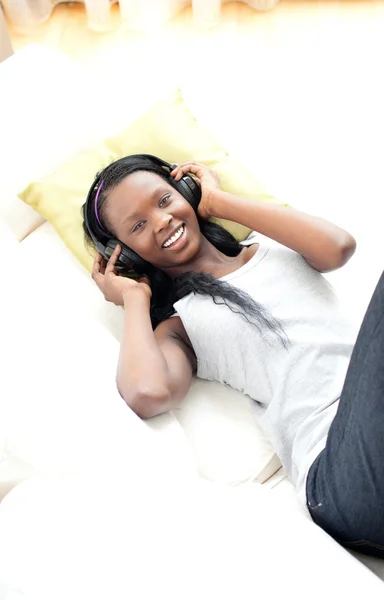 Strahlende Frau hört Musik mit Kopfhörern auf dem Sofa liegend — Stockfoto