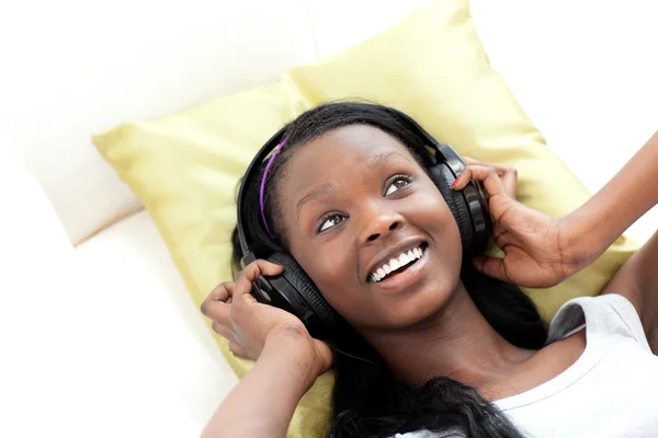 Mujer sonriente escuchando música con auriculares tumbados en un sofá — Foto de Stock