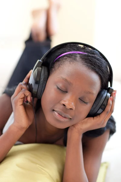 Mujer bonita escuchando música con auriculares tumbados en un sofá —  Fotos de Stock