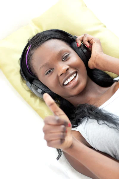 Glad kvinna lyssnar musik med tumme upp liggande på en soffa — Stockfoto