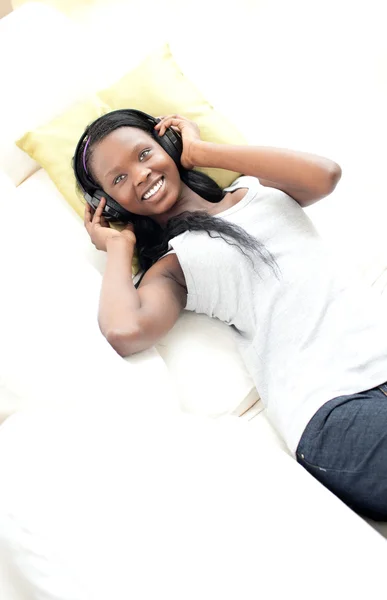 Vrolijke vrouw luisteren muziek met koptelefoon liggen op een sofa — Stockfoto