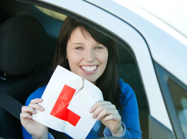 Smiling brunette teen girl sitting in her car tearing a L-sign — Stock Photo, Image