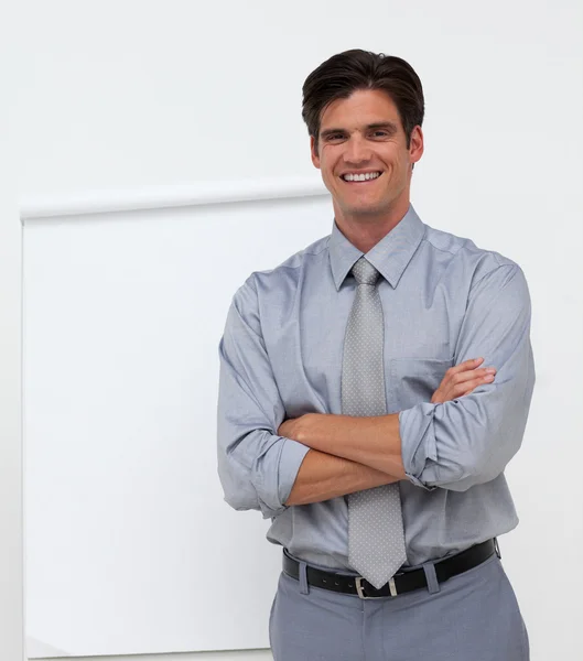 Hombre de negocios sonriente con los brazos cruzados delante de una tabla —  Fotos de Stock