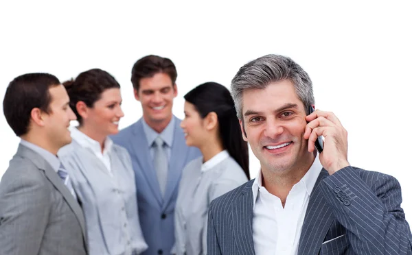 Empresário sorridente ao telefone em pé para além da sua equipa — Fotografia de Stock