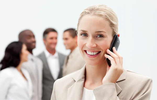 Blonde zakenvrouw op mobiele telefoon met haar team in de achtergrond — Stockfoto