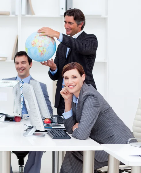 Счастливый менеджер держит глобус со своей командой, работающей за компьютером — стоковое фото