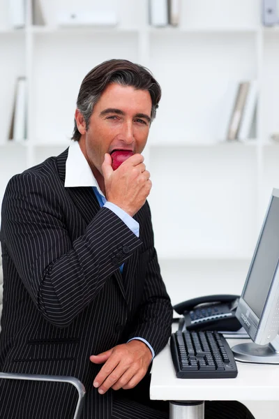Улыбающийся бизнесмен ест яблоко — стоковое фото