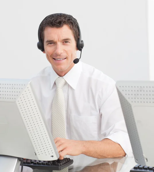 Uomo d'affari sorridente con un auricolare in un call center Fotografia Stock