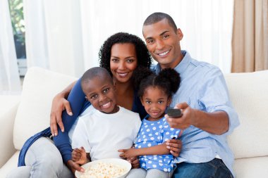 Smiling Afro-american family eating popcorn and watching TV clipart