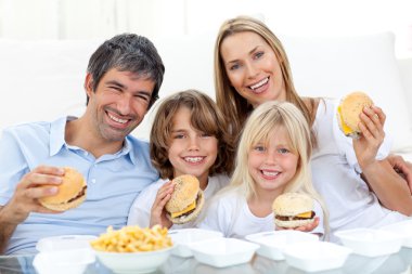 Happy family eating hamburgers sitting on the floor clipart