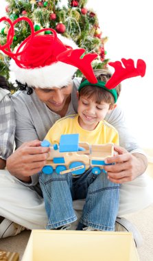 Happy child playing with a train with his father clipart