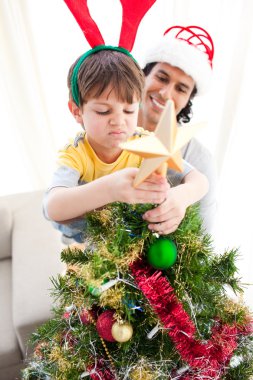 Father and son putting a star on the top of a Christmas tree clipart