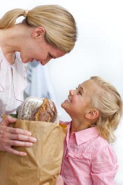 Smiling mother and her daughter unpacking grocery bag clipart