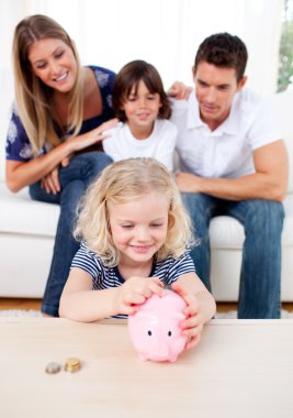 Smiling little girl inserting coin in a piggybank clipart