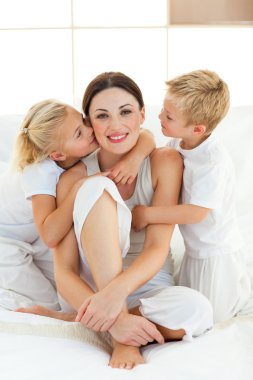 Children kissing their mother sitting on a bed clipart