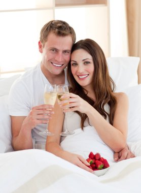 Enamoured couple drinking champagne with strawberries lying in b clipart