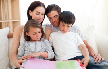 Parents and their children reading a book on the sofa clipart