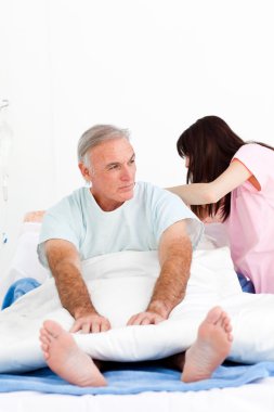 Female nurse adjusting pillows for a senior patient in a hospita clipart