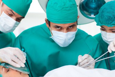 Multi-ethnic surgeons near patient lying on operating table clipart